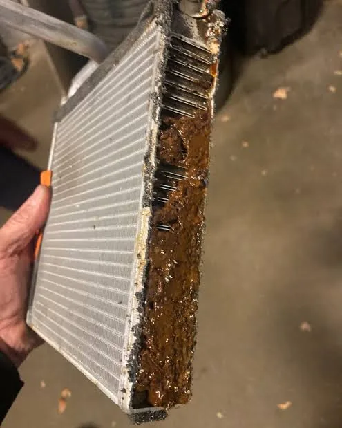 Removed and cut-open truck heater core with heavy sediment accumulation